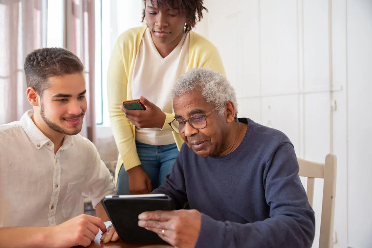 Photo by Kampus Production: https://www.pexels.com/photo/an-elderly-man-in-blue-sweater-holding-a-tablet-while-talking-to-the-people-beside-him-7551607/